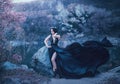 The dark queen pose against the background of gloomy rocks. A luxurious black dress with a long train fluttering in the Royalty Free Stock Photo