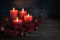 Dark red advent decoration with for lit candles, berrie decoration and Christmas balls against a rustic wooden background, copy