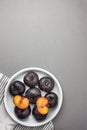 Dark red big plums whole and halved on white vintage enamel plate. White cotton towel on gray stone background. Minimalist style