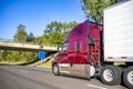 Dark red big rig semi truck with refrigerator semi trailer driving on the wide highway road with bridge across Royalty Free Stock Photo