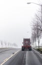 Dark red big rig semi truck tractor moving ahead on foggy winter road with trees on the sides Royalty Free Stock Photo