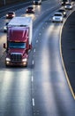 Dark red big rig semi truck transporting cargo in refrigerator semi trailer running on the wide multilines highway at night with Royalty Free Stock Photo