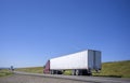 Dark red big rig semi truck transporting commercial cargo in dry van semi trailer driving on the narrow road with hill on the side Royalty Free Stock Photo