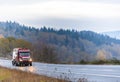 Dark red big rig towing semi truck tow broken day cab semi truck on the winding wet rainy autumn road in twilight Royalty Free Stock Photo