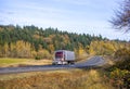 Classic dark red big rig semi truck transporting frozen cargo in refrigerated semi trailer running on the winding road with autumn Royalty Free Stock Photo