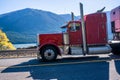 Red classic big rig semi truck with chrome parts driving on the road along the river Royalty Free Stock Photo