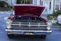 A dark red classic car with the hood up at an outdoor car show