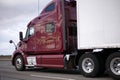 Dark red professional big rig semi truck with trailer on the road delivering commercial cargo Royalty Free Stock Photo