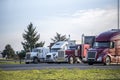 Dark red and white big rigs semi trucks with different semi trailers standing in row on industrial city parking lot for truck Royalty Free Stock Photo