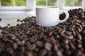 Dark roasted coffee beans piled and scattered with a small white ceramic espresso cup