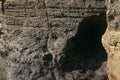 Dark rock of volcanic lava on the Indian Ocean coast of Bali. A small cave excavated into a cliff wall by a sea surf. Sun rays Royalty Free Stock Photo