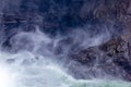 dark rock and white water from waterfall make shapes and mist in the air