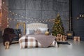 A dark room with a bed and many decorations and lights, a Christmas tree with gifts under it, a gray wall