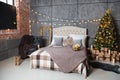 A dark room with a bed and many decorations and lights, a Christmas tree with gifts under it, a gray wall