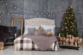 A dark room with a bed and many decorations and lights, a Christmas tree with gifts under it, a gray wall Royalty Free Stock Photo