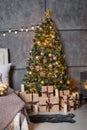 A dark room with a bed and many decorations and lights, a Christmas tree with gifts under it, a gray wall Royalty Free Stock Photo