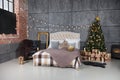 A dark room with a bed and many decorations and lights, a Christmas tree with gifts under it, a gray wall Royalty Free Stock Photo