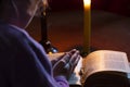 A dark room, a candle is burning. Book. On the table is a cross. The girl folded her arms over the book. There is a tint Royalty Free Stock Photo