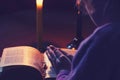 A dark room, a candle is burning. Book. On the table is a cross. The girl folded her arms over the book. There is a tint Royalty Free Stock Photo