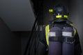 In a dark room, close-up of the back of a firefighter in protective clothing and a helmet with a flashlight