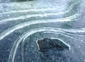 Dark, rugged rock formation standing amidst frozen landscape of icy curves and snow. Contrast of black, white, and blue