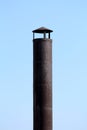 Dark rusted metal industrial chimney with improvised cap on top