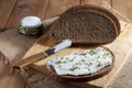 Dark rye bread, sandwich with cream and knife on wooden cutting board and salt in saltshaker on burlap