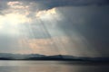 Dark sea and cloudy sky with sun rays lightning through the clouds. Green hills and mountains on the horizon. Landscape and seasca Royalty Free Stock Photo