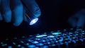 A gloved hand uses a flashlight to reveal fingerprints on a dark keyboard. Royalty Free Stock Photo