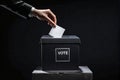 Dark side ballot box with hand person vote on blank voting slip at dark background. Royalty Free Stock Photo