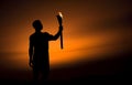 Dark silhouette of an athlete holding the Olympic flame against the backdrop of sunset. Royalty Free Stock Photo