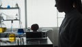 Dark silhouette of a female scientist sitting at a table in front of an apple, a syringe, and an ampoule of a chemical