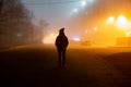 The dark silhouette of a human stands in the fog against the background of the lights of the houses and trees Royalty Free Stock Photo