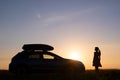 Dark silhouette of lonely woman relaxing near her car on grassy meadow enjoying view of colorful sunrise. Young female driver Royalty Free Stock Photo