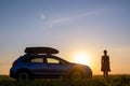 Dark silhouette of lonely woman relaxing near her car on grassy meadow enjoying view of colorful sunrise. Young female driver Royalty Free Stock Photo