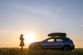 Dark silhouette of lonely woman relaxing near her car on grassy meadow enjoying view of colorful sunrise. Young female Royalty Free Stock Photo