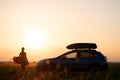 Dark silhouette of lonely woman relaxing near her car on grassy meadow enjoying view of colorful sunrise. Young female Royalty Free Stock Photo