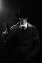 A dark silhouette of a male detective in a coat and hat with a gun in his hands in the Noir style. The head is lowered Royalty Free Stock Photo