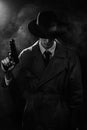 A dark silhouette of a male detective in a coat and hat with a gun in his hands in the Noir style. The head is lowered
