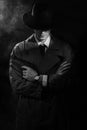 A dark silhouette of a male detective in a coat and hat with a gun in his hands in the Noir style. The head is lowered Royalty Free Stock Photo