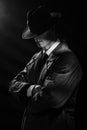 a dark silhouette of a man in a raincoat and hat with his head down in the style of crime noir. A dramatic noir portrait