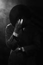 a dark silhouette of a man in a raincoat and a hat in the style of crime noir. Dramatic noir portrait in the style of