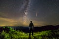 Dark silhouette of a man standing in mountains at night enjoying milky way and Neowise comet with light tail in dark sky view Royalty Free Stock Photo