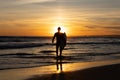 Dark silhouette of a man surfer walking out on the seashore holding a surfboard at bright sunset Royalty Free Stock Photo