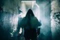 Dark silhouette of strange danger man in hood in back light with smoke or fog in scary grunge corridor or tunnel Royalty Free Stock Photo