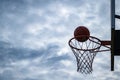 Dark silhouette of street basketball ball falling into the hoop on a cloudy day. Close up of a ball above the hoop net. Concept of Royalty Free Stock Photo