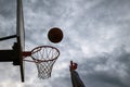 Dark silhouette of street basketball ball falling into the hoop on a cloudy day. Close up of a ball above the hoop net. Concept of Royalty Free Stock Photo