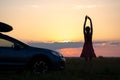 Dark silhouette of woman driver standing near her car on grassy field enjoying view of bright sunset. Young female relaxing during Royalty Free Stock Photo