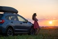 Dark silhouette of woman driver standing near her car on grassy field enjoying view of bright sunset. Young female relaxing during Royalty Free Stock Photo