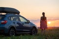 Dark silhouette of woman driver standing near her car on grassy field enjoying view of bright sunset. Young female Royalty Free Stock Photo